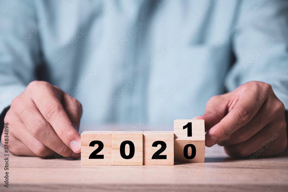 Naklejka premium Businessman flipping wooden cubes block to change 2020 to 2021 year on wooden table. Happy new year and start new business concept.