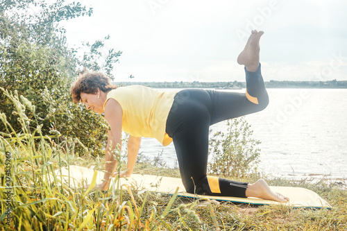 Senior woman making yoga and pilates near river in summer. Lockdown concept, sport alone. photo