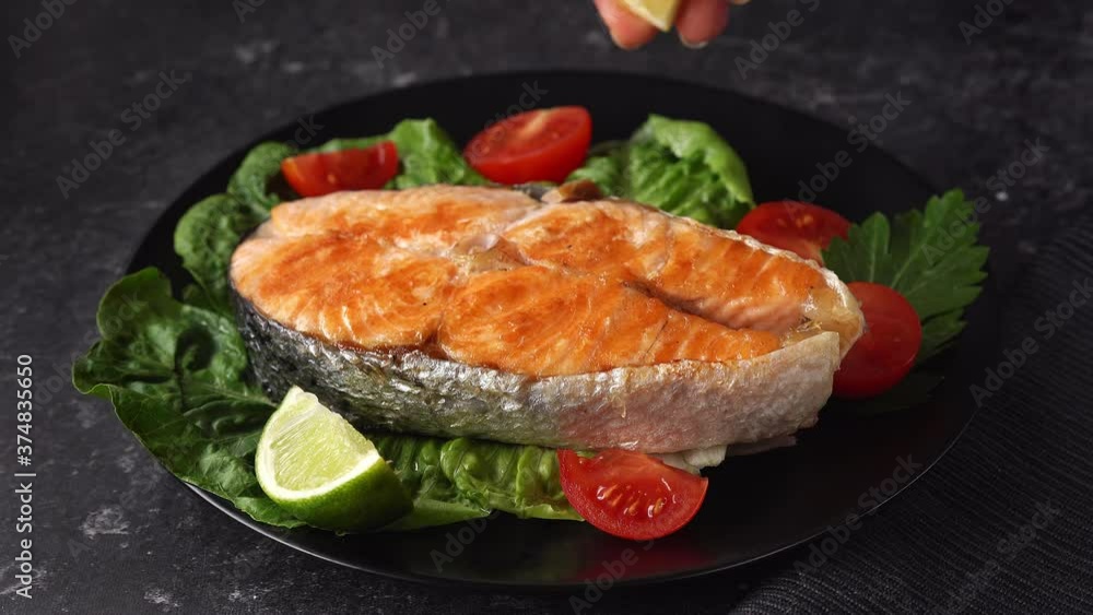 Close up of female hand sprinkling a lemon juice on grilled salmon steak. Black background. 4K UHD Close up of female hand sprinkling a lemon juice on grilled salmon steak. Black background. 4K UHD