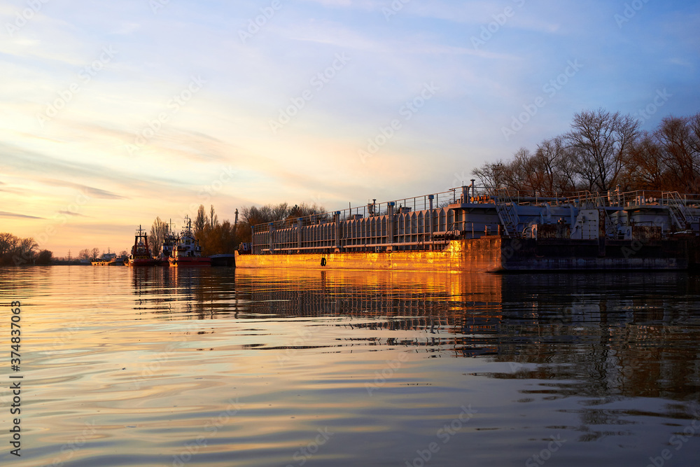 Lage barge (bulk carrier) with tankers near the pier at sunset in autumn river