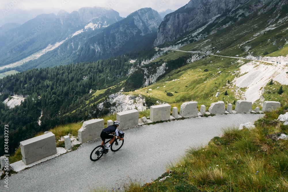 Fototapeta premium Professional road cyclist on training trip in alps. Amazing epic landscape of mountain road and cyclist on travel tour bike descends steep hill. Inspiring photo of cycling sport