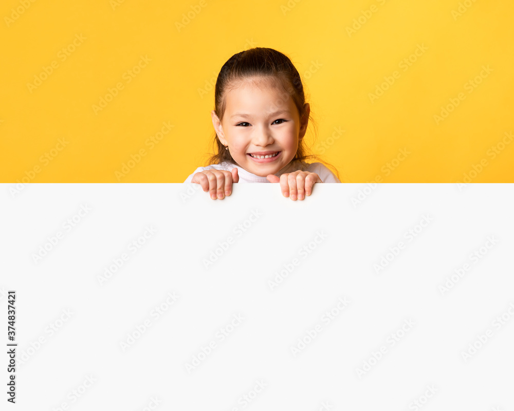 Asian girl hiding behind blank white advertising billboard Asian girl hiding behind blank white advertising billboard