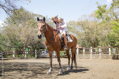 Beautiful young woman riding a horse with her little toddler girl, summer time outdoor activity © triocean