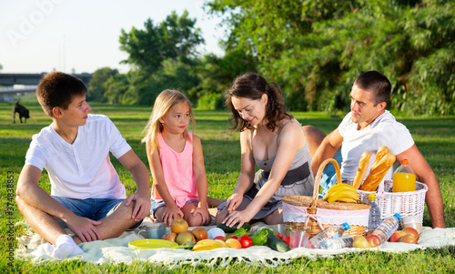 Happy family with two children enjoying picnic on green meadow together..