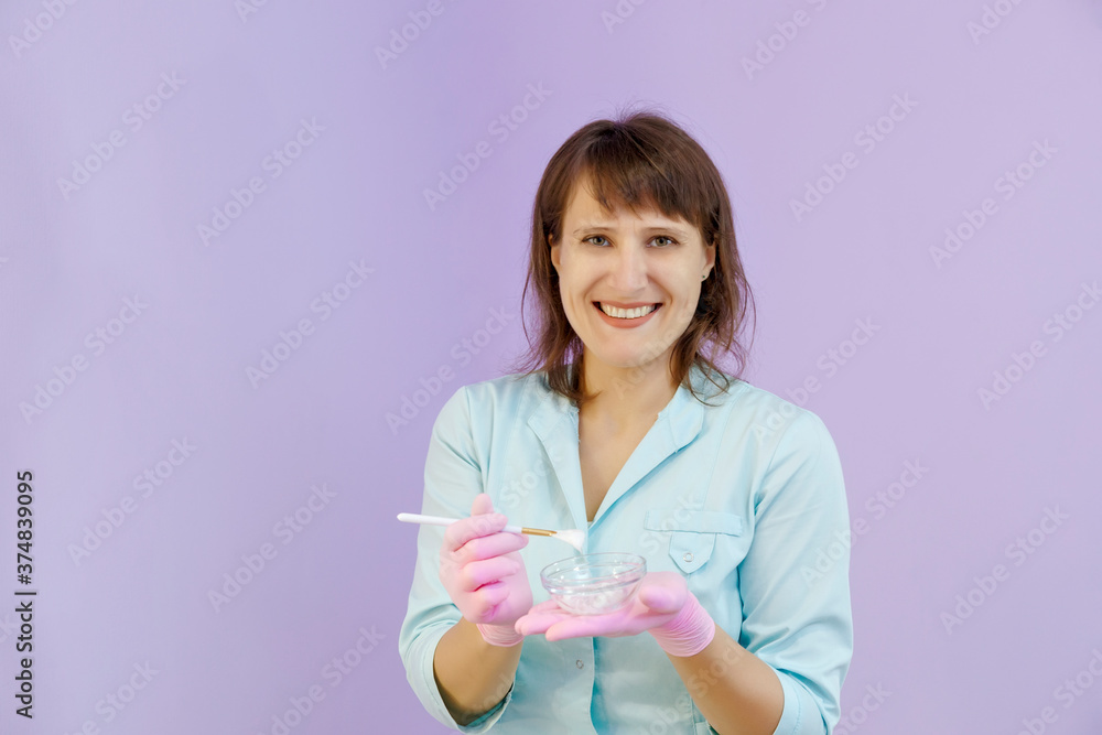 Attractive woman in green uniform and pink gloves smiling with a cup of a facial cream in her hands Attractive woman in green uniform and pink gloves smiling with a cup of a facial cream in her hands