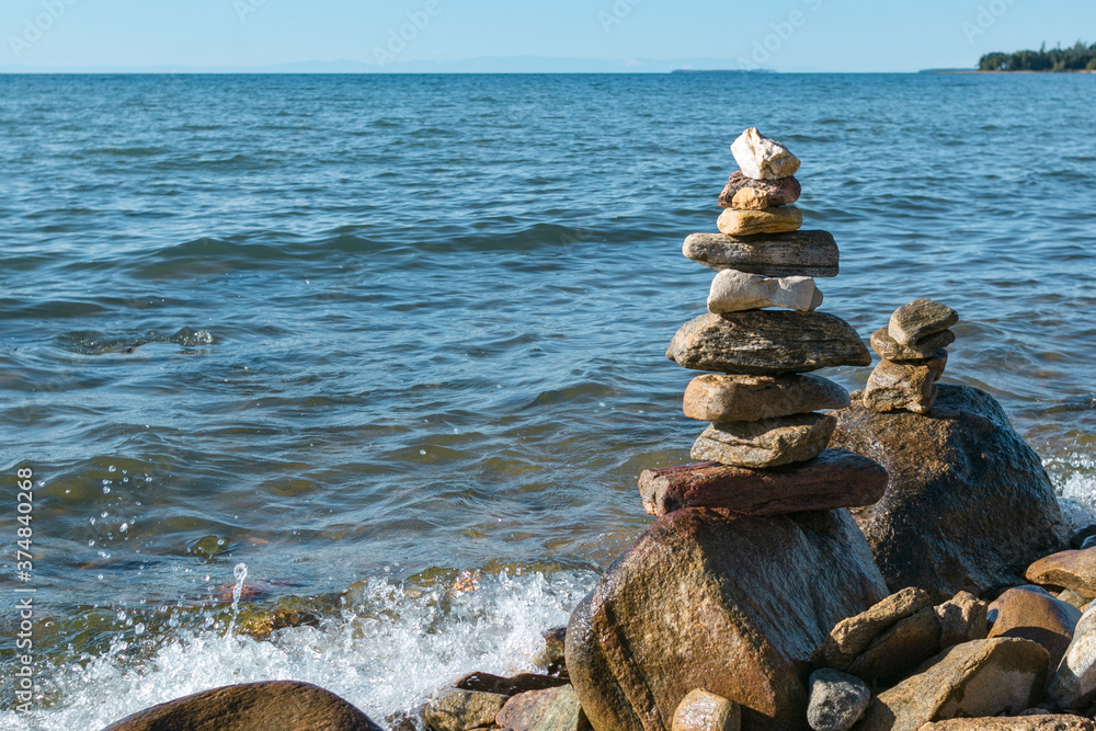 Pyramids of stacked stones on boulder on the inshore waves of Lake Baikal, scenic seascape, balance and harmony concept Pyramids of stacked stones on boulder on the inshore waves of Lake Baikal, scenic seascape, balance and harmony concept