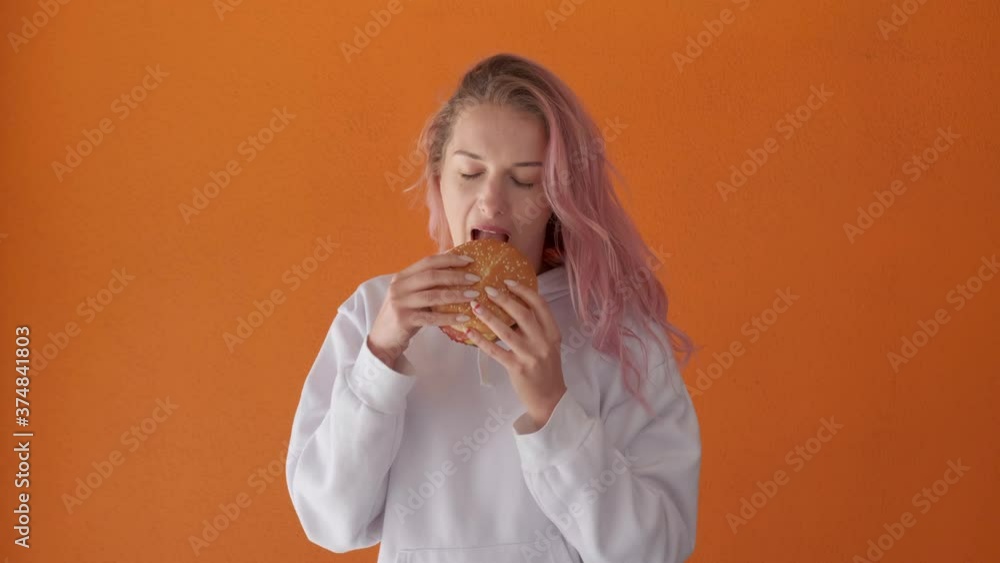 Young woman with appetite to eat big tasty burger. Enjoyment of food. Orange background. Young woman with appetite to eat big tasty burger. Enjoyment of food. Orange background.