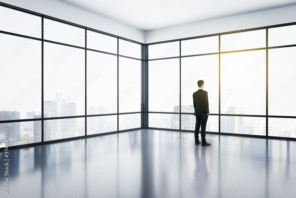 Businessman standing in modern office interior with panoramic city view.