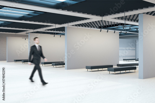 Businessman walking in exhibition hall interior with copyspace on concrete walls © Who is Danny