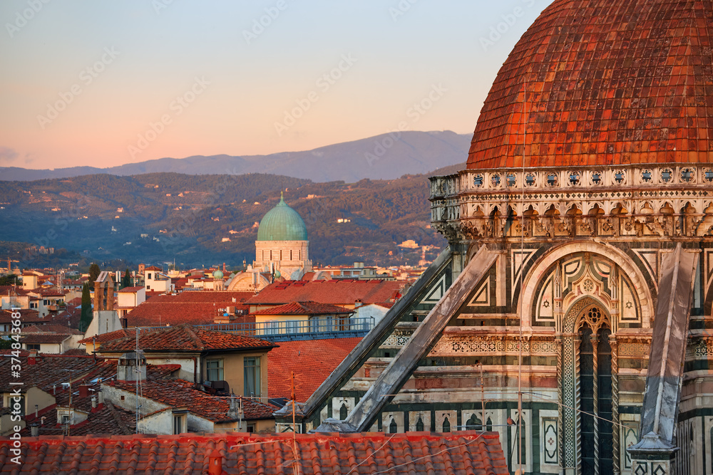 Fototapeta premium Cathedral of Saint Mary of the Flower in Florence. Tourist hotspot in Tuscany. Aerial view of a gothic dome and medieval city in background, illuminated by setting sun. UNESCO World Heritage Site.