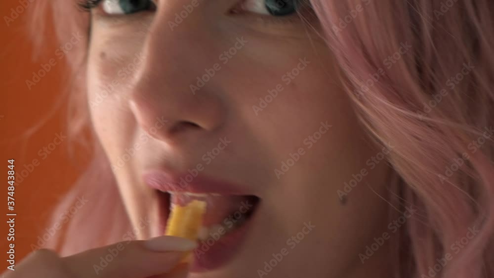 The lips of a young woman who eats a fried potato. Enjoyment of food. Orange background. Pink hair. The lips of a young woman who eats a fried potato. Enjoyment of food. Orange background. Pink hair.
