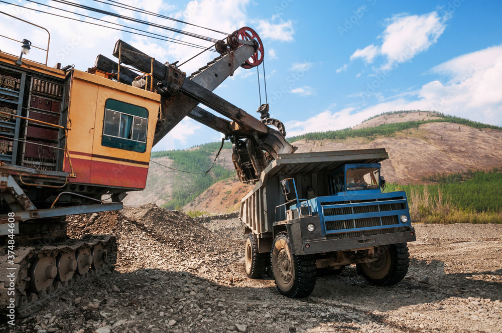Excavator loads mountain soil into a dump truck bucket