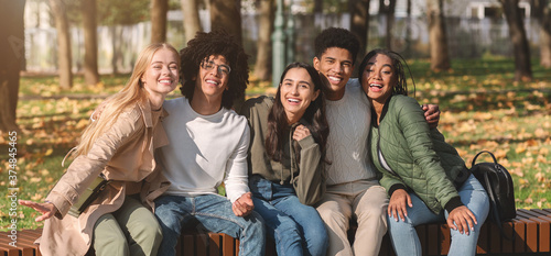 Panoramic photo of joyful multiracial teenagers resting in park
