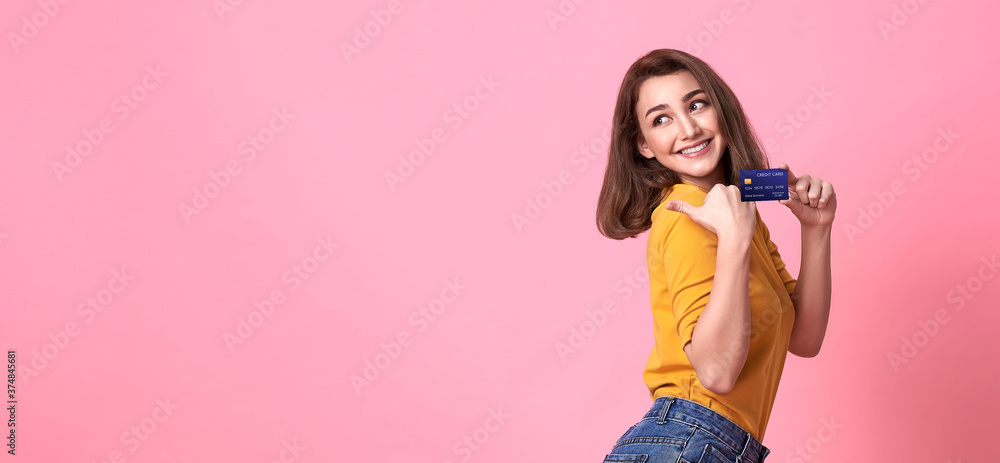 Young woman holding credit card in casual yellow shrit with gorgeous in trust and confidence for money transaction isolated on bright pink background. Young woman holding credit card in casual yellow shrit with gorgeous in trust and confidence for money transaction isolated on bright pink background.