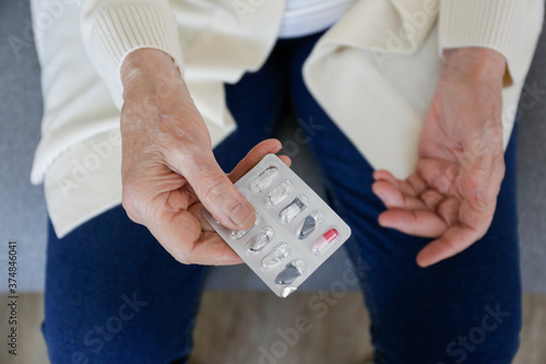 Top view shot of senior lady holding the blister with one last pill. Old age woman wearing beige cardigan and denim pants with just one capsule. Close up, copy space, background.