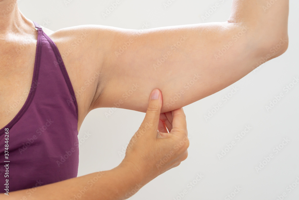 Mature woman pinching flabby arm, body care and fitness concept