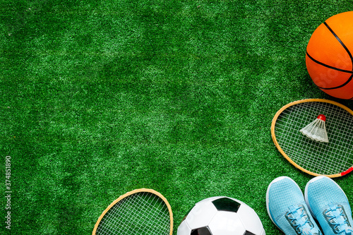 Sport balls and badminton rackets on football grass. Top view copy space