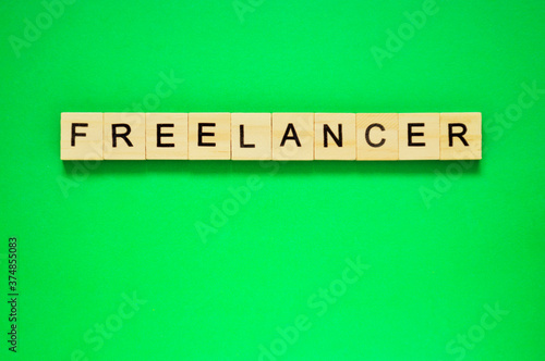 Word freelancer. Wooden blocks with lettering on top of green background. Top view of wooden blocks with letters on green surface