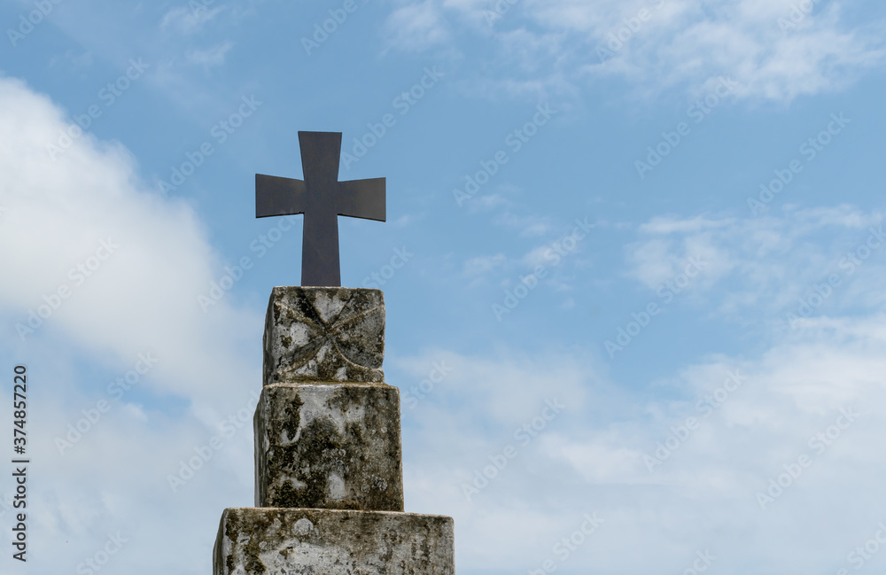 Beautiful photo of holy cross fixed on top of old and dusty cement pillar with clear blue sky and sparse white clouds in background. Concept of haunting, exorcism, belief, church, jesus, cemetery etc.