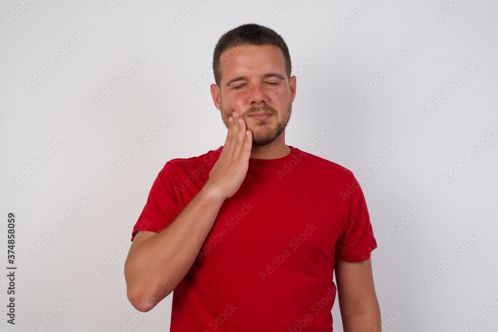 Young caucasian man wearing red t-shirt over white background touching mouth with hand with painful expression because of toothache or dental illness on teeth. Young caucasian man wearing red t-shirt over white background touching mouth with hand with painful expression because of toothache or dental illness on teeth.