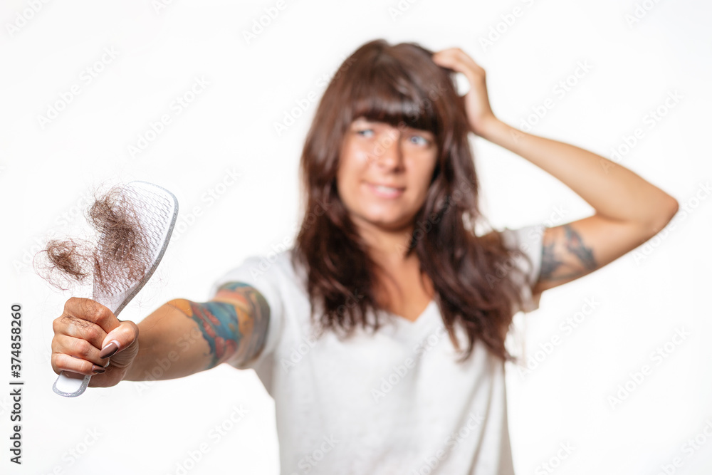 A blurred portrait of tattooed woman holds a comb with her hair pulled out, and holds her head in amazement. White background. Hair care concept A blurred portrait of tattooed woman holds a comb with her hair pulled out, and holds her head in amazement. White background. Hair care concept