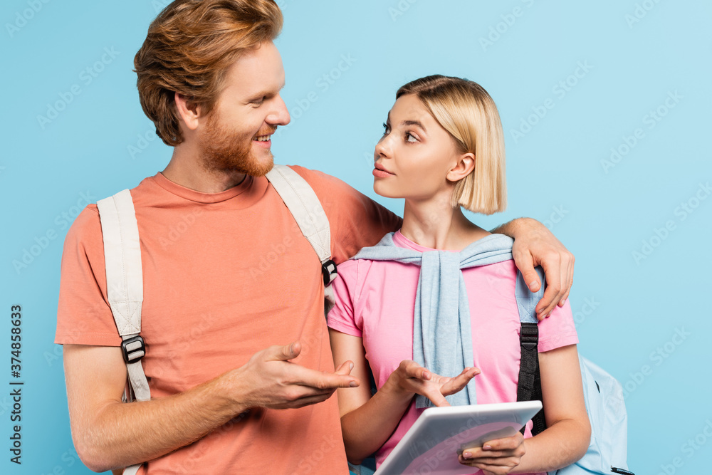 young students looking at each other while pointing with fingers at digital tablet on blue young students looking at each other while pointing with fingers at digital tablet on blue