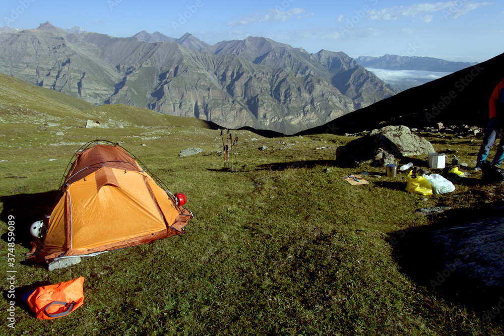 Tourist tents, backpacks, trekking poles and a camping kitchen against the backdrop of the mountains on a sunny morning. Tourist camp in the mountains.