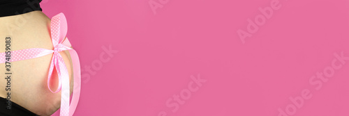 Pink bow on pregnant belly, horizontal banner, copy space for text © Michael