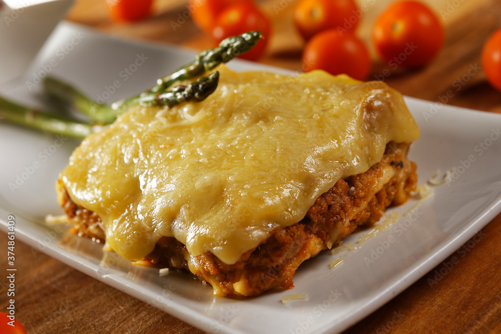 Beef lasagna with cheese in red tomato sauce and asparagus.