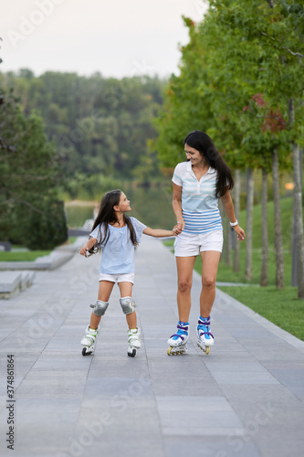 Young mother and her little daughter rollerskating in summer park. happy family have fun