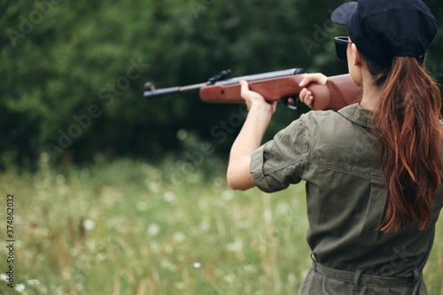 Woman soldier holding weapon in hand aiming hunting weapons green trees 