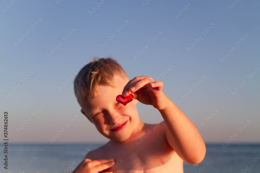 Red glass heart on the background of the sea in the hand of a child. Children's vacation by the ocean. happy boy on vacation on the beach.