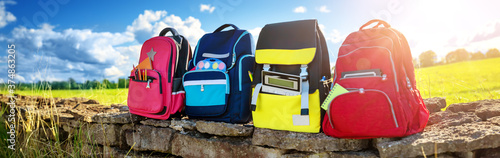 Colourful children schoolbags outdoors on the field photo