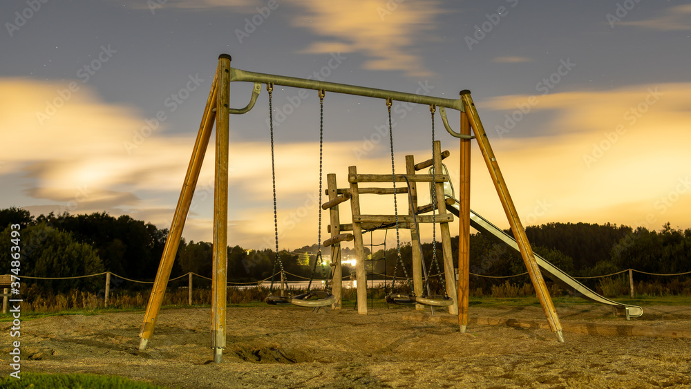 Metalowe huśtawki na drewnianej konstrukcji na tle gwieździstego nocnego nieba Metalowe huśtawki na drewnianej konstrukcji na tle gwieździstego nocnego nieba
