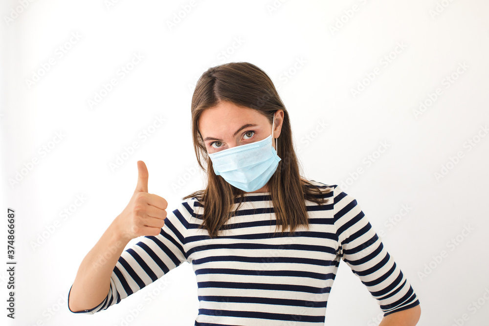 Woman showing thumb up. Beautiful caucasian young woman with disposable face mask. Protection versus viruses and infection. Studio portrait, concept with white background Woman showing thumb up. Beautiful caucasian young woman with disposable face mask. Protection versus viruses and infection. Studio portrait, concept with white background