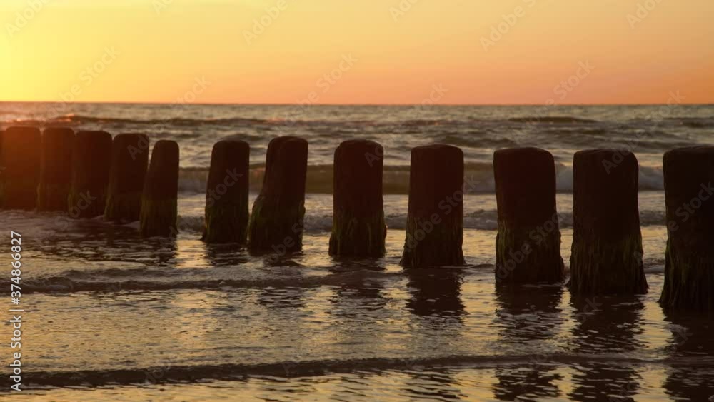 Wooden poles at the beach at golden sunset. Wave breaker pole heads in ocean water waves. Wooden poles at the beach at golden sunset. Wave breaker pole heads in ocean water waves.
