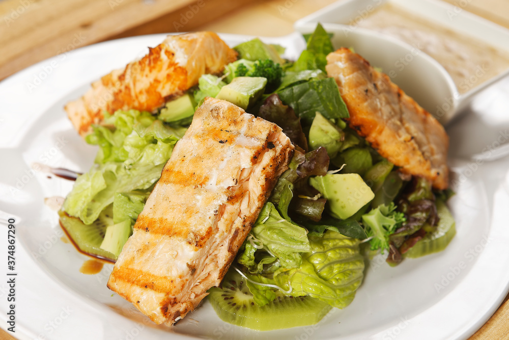 Tilapia fish fillet salad with lettuce, cabbage, kiwi, broccoli, and avocado.