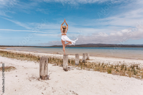 Obraz na plátně Beautiful woman balance on wooden post yoga pose in swimwear and sarong