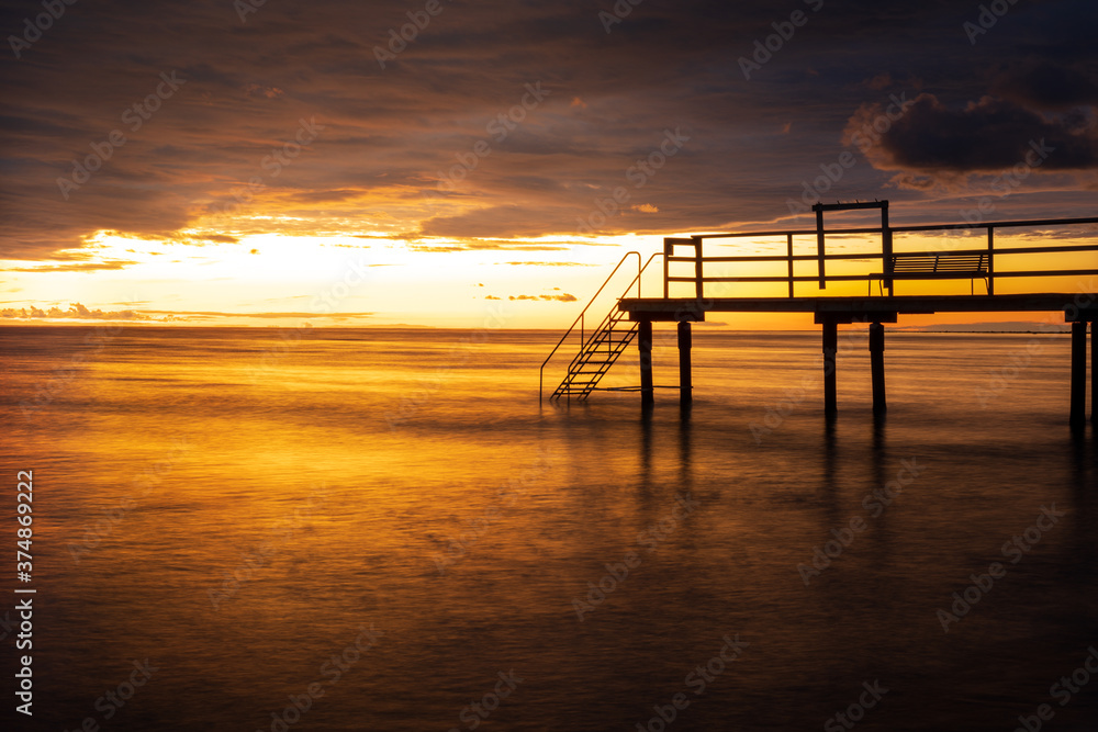 Bathing jetty with reflection in the ocean during golden sunset in south Sweden. Selective focus.