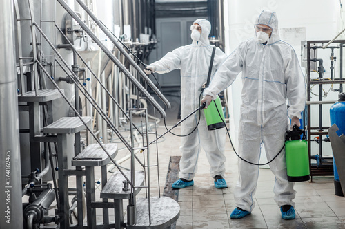 Konstfotografi Guys in protective suits and glasses disinfect with spray bags to factory
