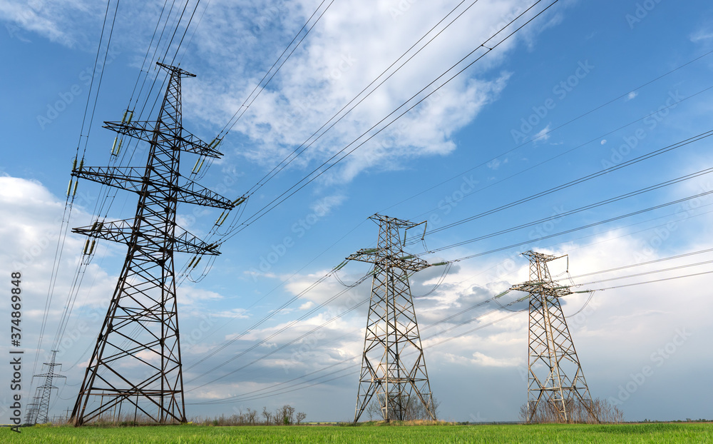 Pylons of electrical net on a panorama of blue cloudy sky and green meadow Pylons of electrical net on a panorama of blue cloudy sky and green meadow