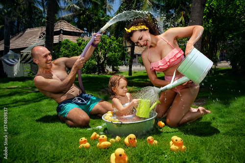 Father Pours Water Over wifes Head and  Mother Pours Water from watering can on baby in basin with many ducks. Family playing and take a bath by their garden