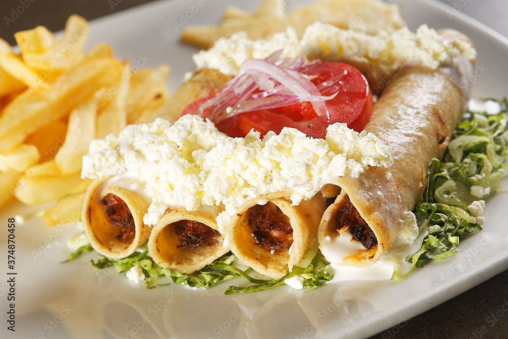 Golden chicken tacos with lettuce, fresh cheese and tomato accompanied by french fries.