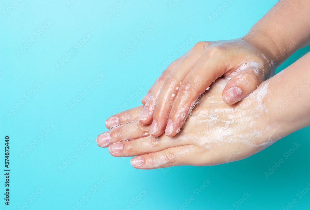 Fototapeta premium The girl washes her hands with soap and foam on blue background