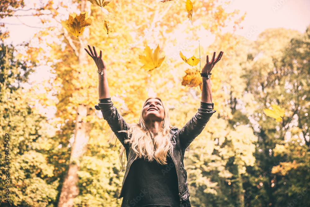 Woman in a park throwing yellow leafs in the air