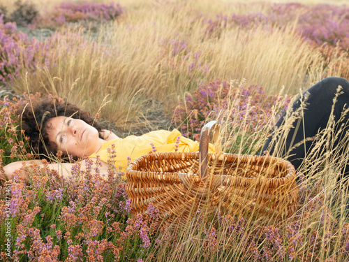 Une jeune femme est allongée dans une prairie aux couleurs automnale à coté d'un panier en châtaignier. photo