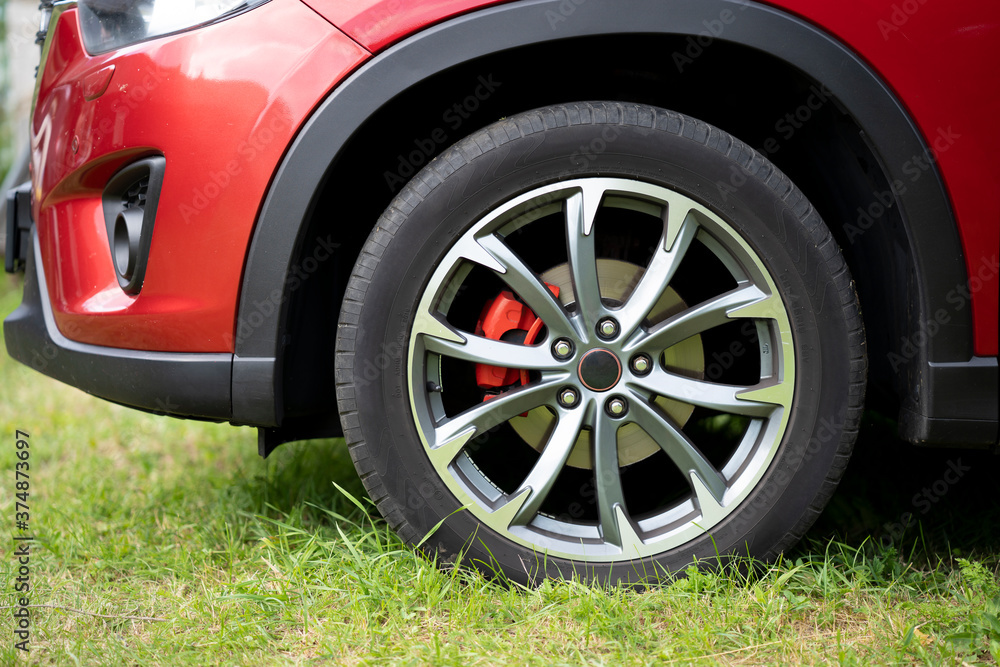The front wheel of a red car, which is parked in the wrong place on the grass.