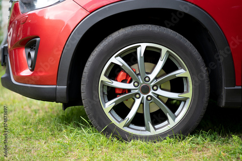 The front wheel of a red car, which is parked in the wrong place on the grass. © dimetradim