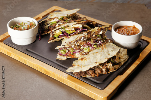 Traditional Oaxacan tlayuda stuffed with meat, melted cheese and avocado, accompanied by red chili sauce.