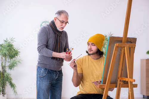 Young man taking lesson from old painter